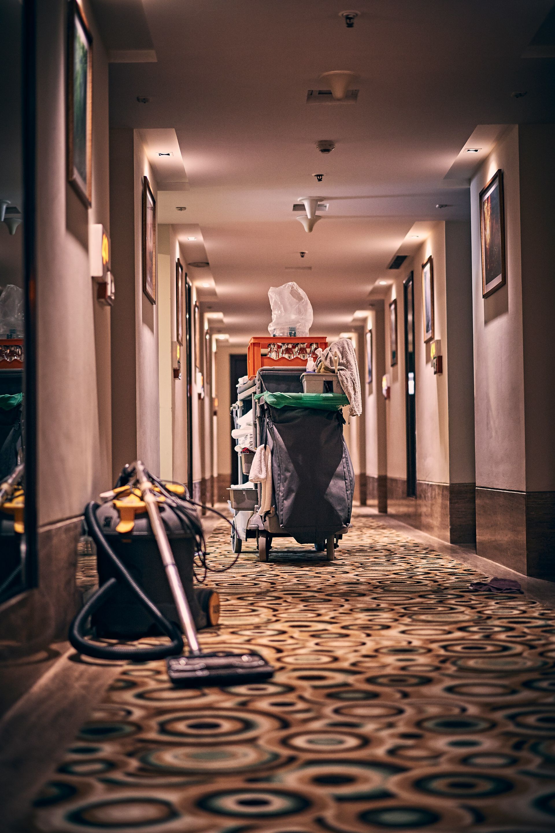 A vacuum cleaner is sitting on the floor in a hallway next to a trash can.