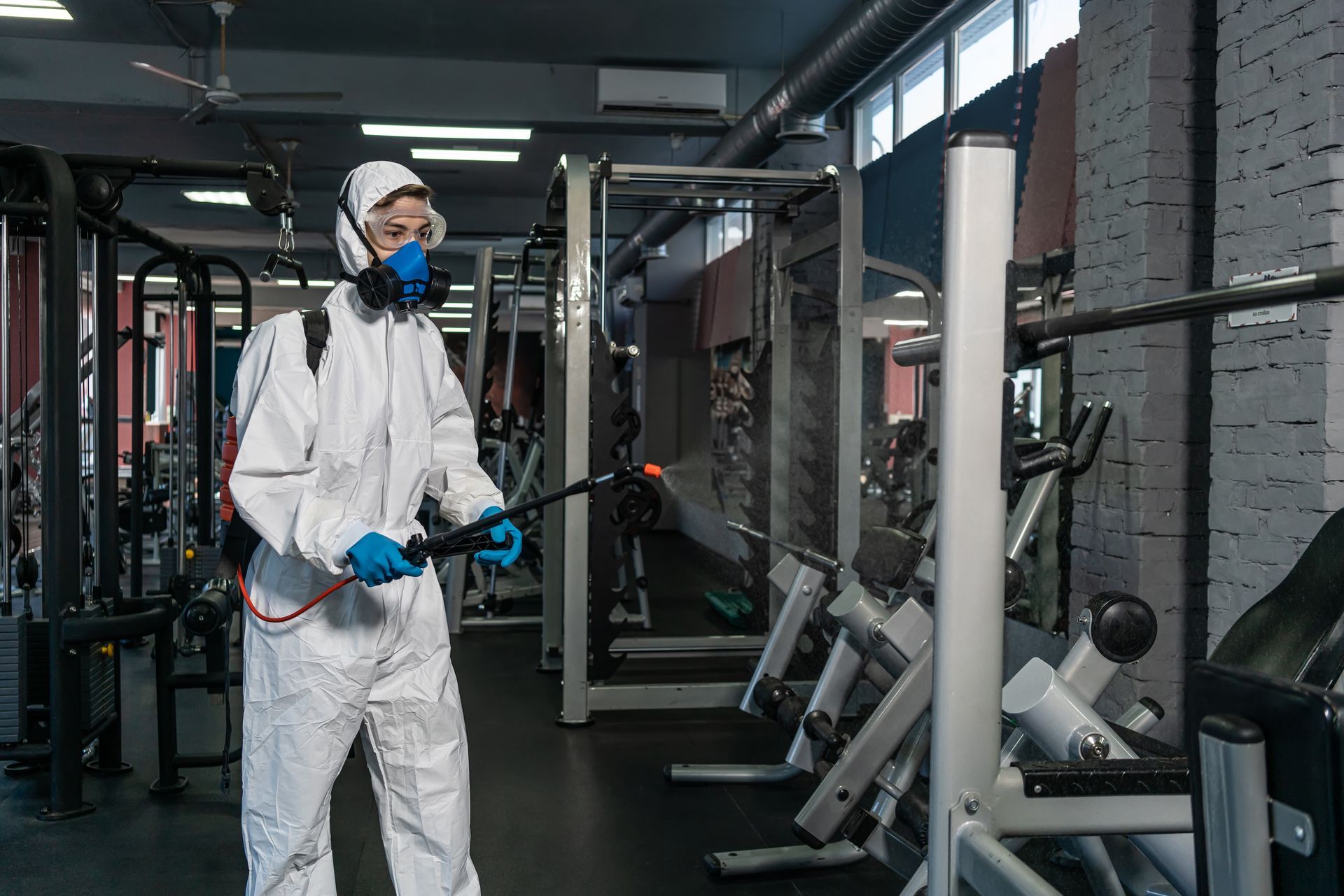 A man in a protective suit is disinfecting a gym.