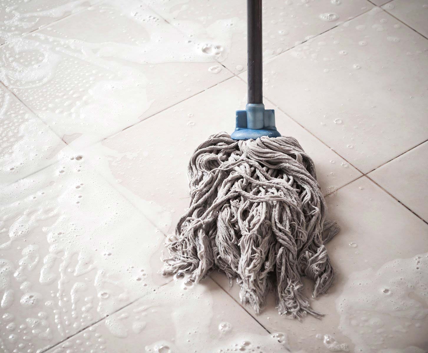 A mop with a blue handle is sitting on a tiled floor.