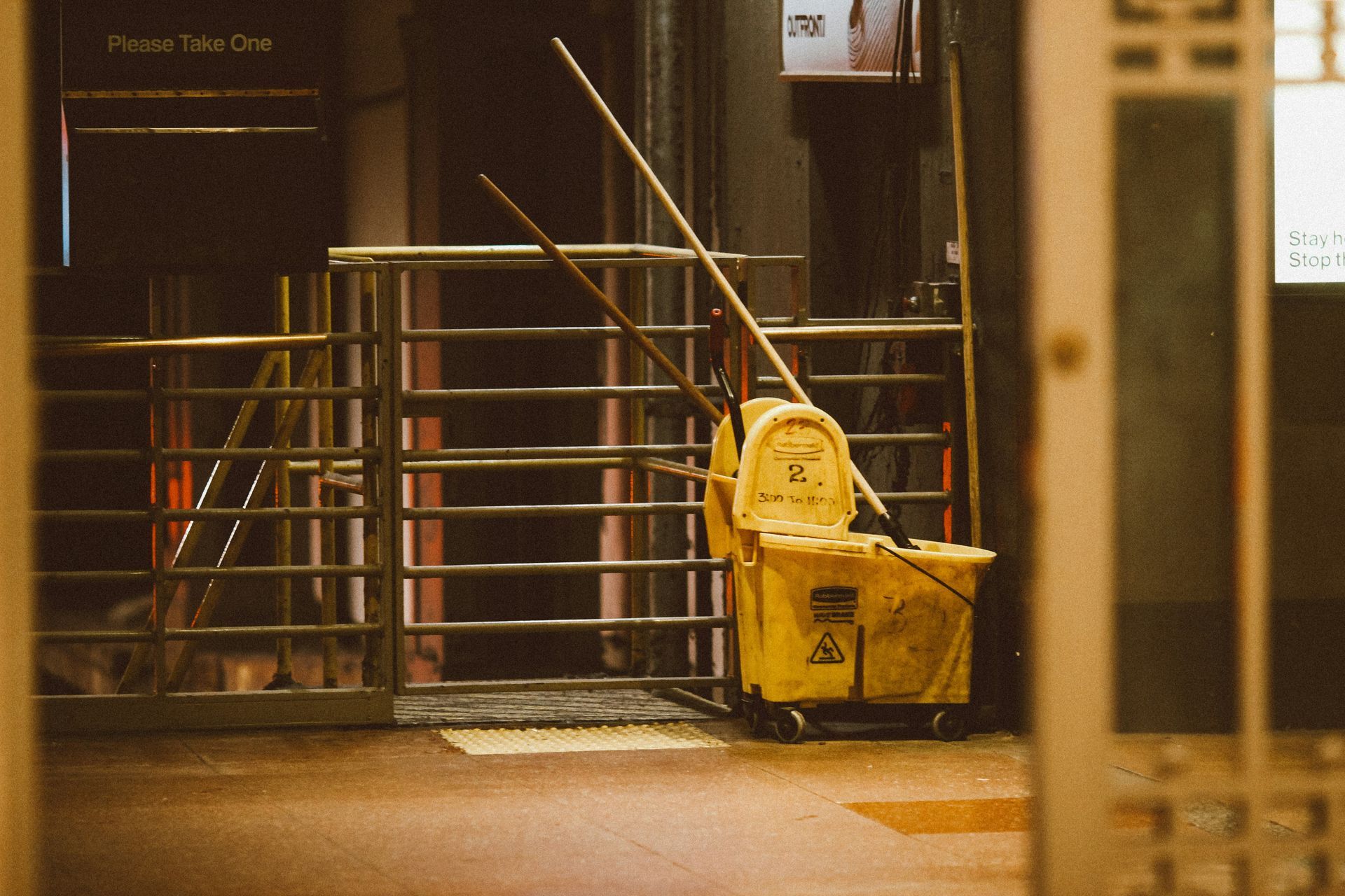 A yellow mop bucket is sitting in a hallway next to a fence.