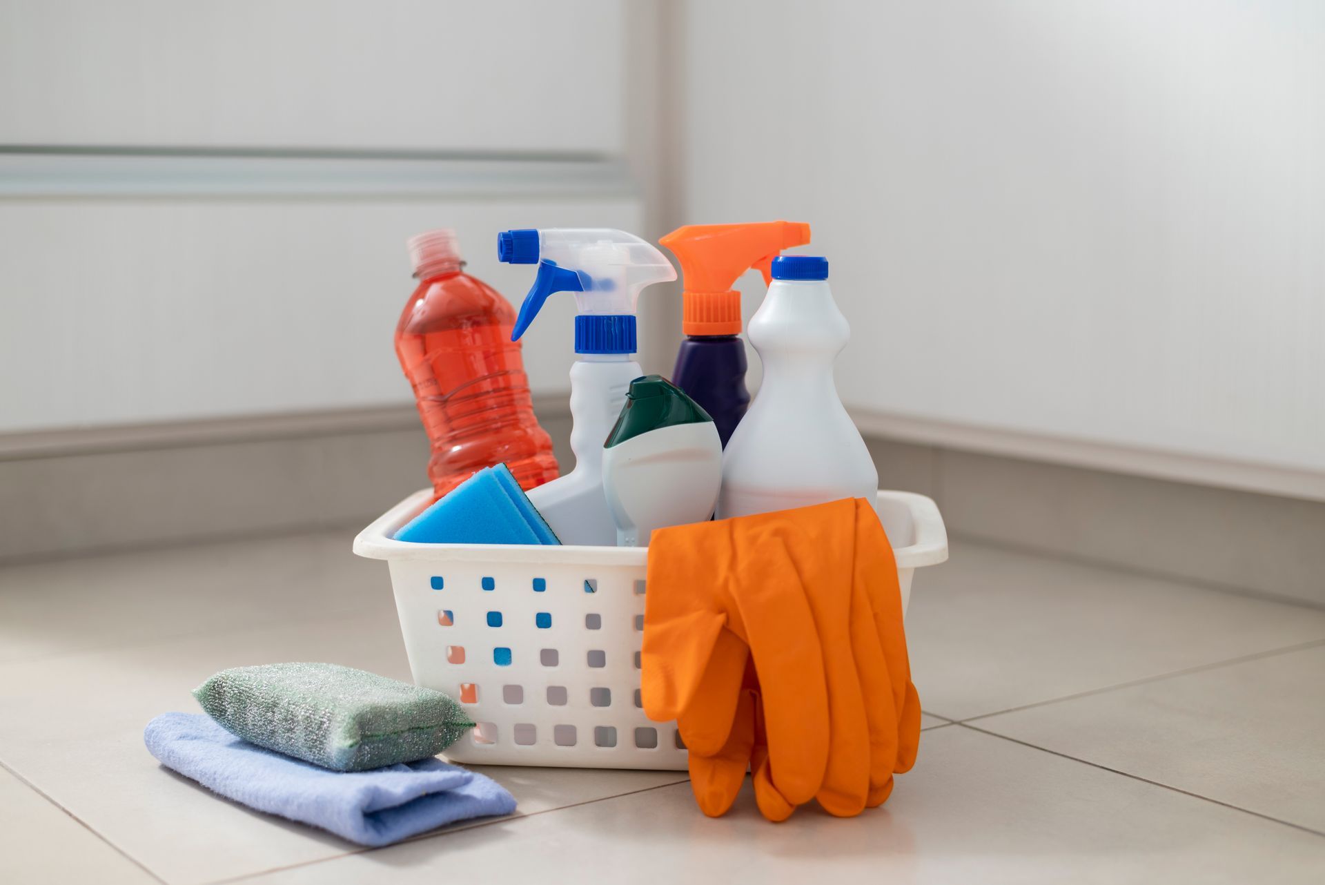 A basket filled with cleaning supplies and gloves on the floor.