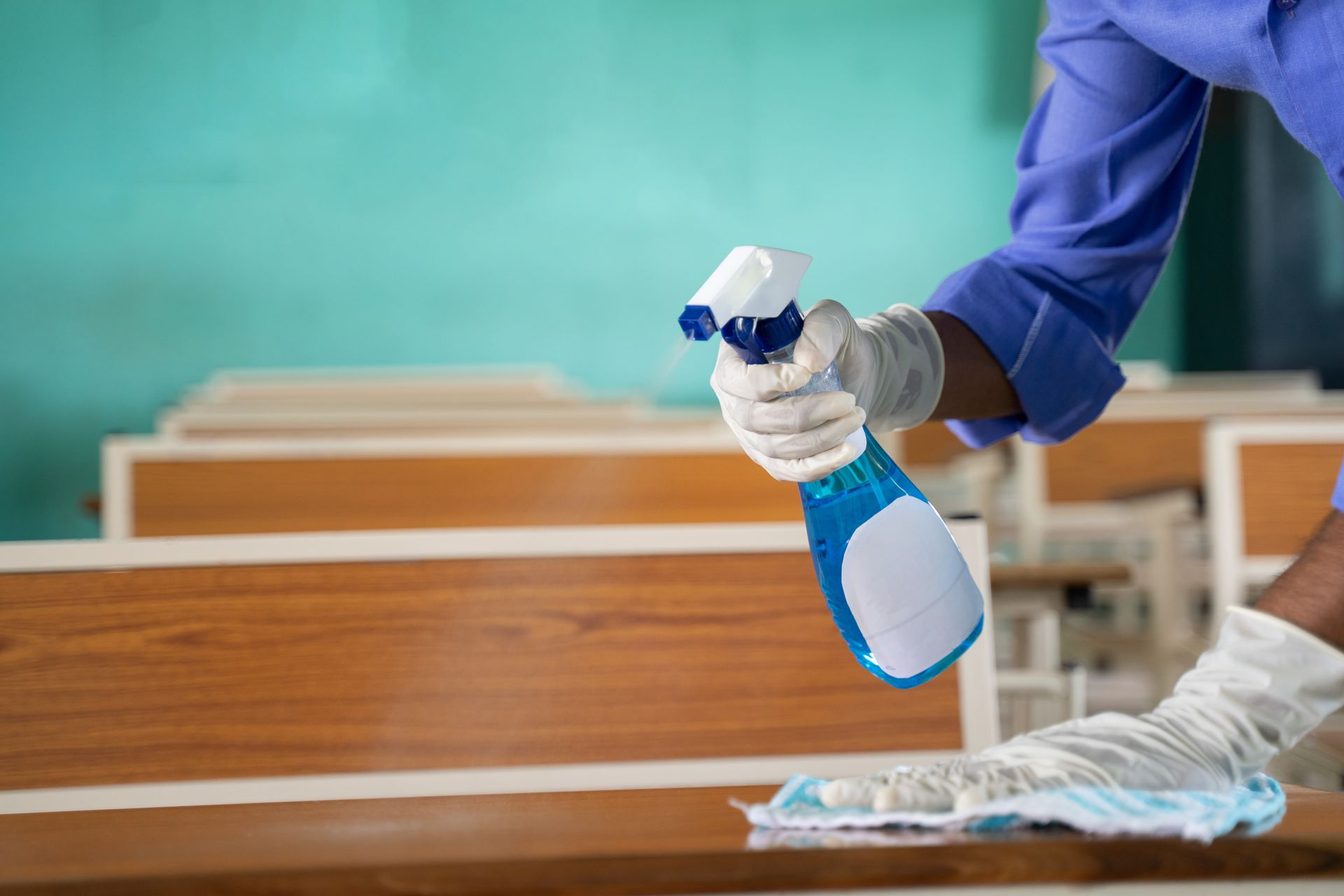 A person is cleaning a desk with a spray bottle and a cloth.