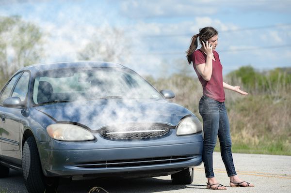 Woman on phone beside car with steam billowing from under the hood on a rural road. | Dave's Automotive LLC