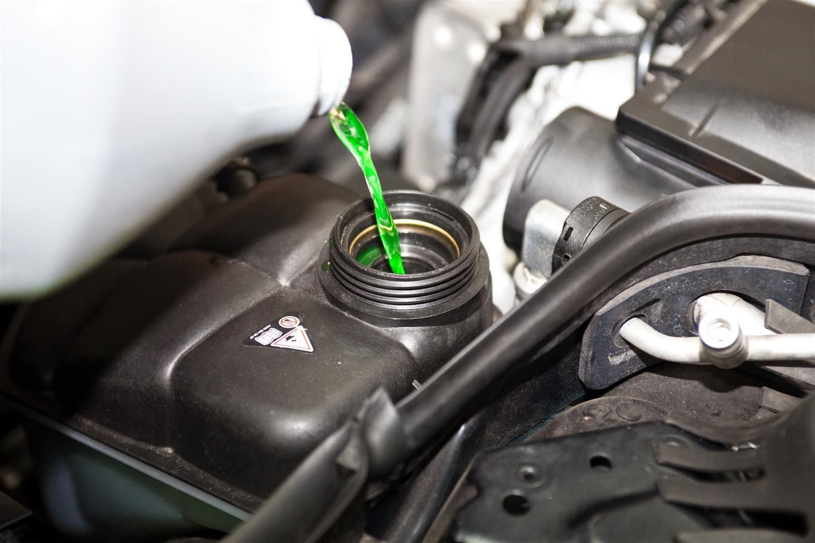 Green coolant being poured into a black reservoir in a car engine compartment. | Dave's Automotive LLC