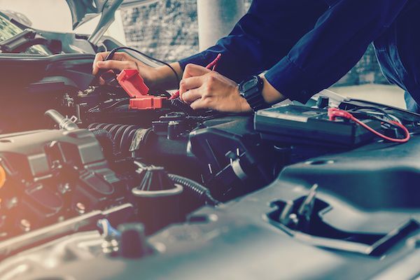 Person checking car engine with jumper cables. | Dave's Automotive LLC