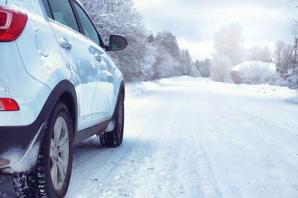 White car on snowy road, winter scene with trees and sunlight. | Dave's Automotive LLC