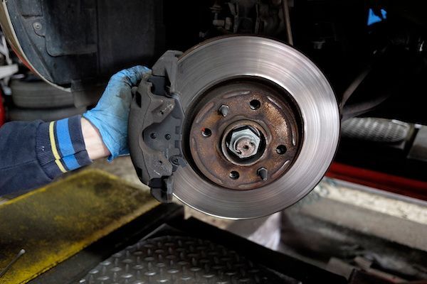 Mechanic's gloved hand holding a car brake caliper and rotor; in a garage setting. | Dave's Automotive LLC
