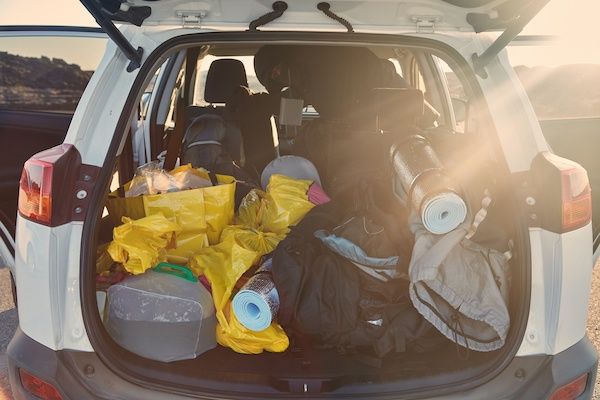 A white car trunk packed with camping gear and a person reaching inside, in bright sunlight. | Dave's Automotive LLC
