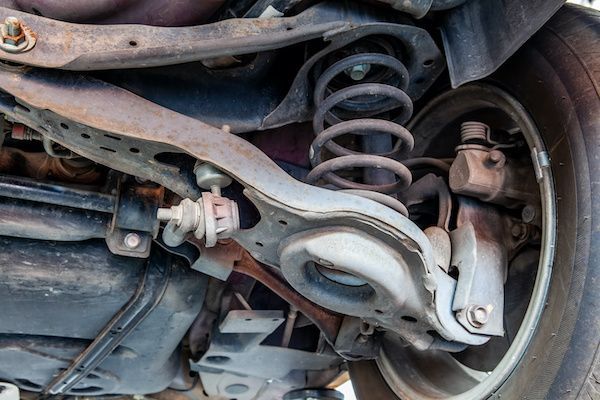 Underside of a car with suspension components visible: coil spring, control arms, shock absorber, and wheel. | Dave's Automotive LLC
