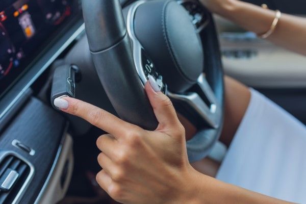 Woman's hand on steering wheel, pointing to a button on the side. Inside a car. | Dave's Automotive LLC