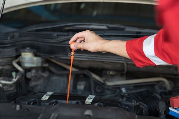 Mechanic in red uniform checking car oil with dipstick under the hood. | Dave's Automotive LLC