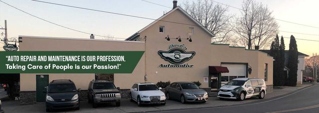 Cars parked in front of an auto repair shop with a green banner and logo on the building. | Dave's Automotive LLC