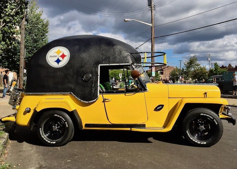 Yellow Jeep modified with a Pittsburgh Steelers helmet roof, parked on a city street. | Dave's Automotive LLC