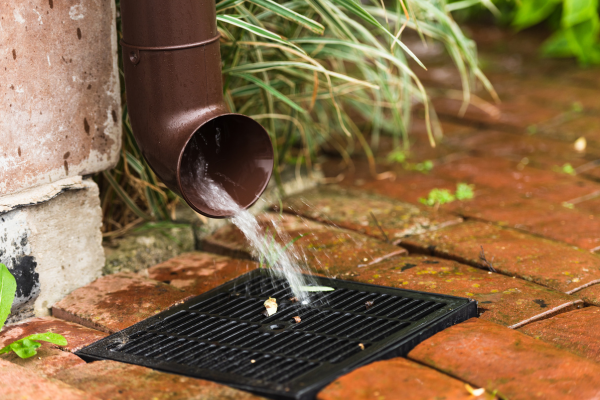 Brown gutter draining water into a black grate on a brick patio.