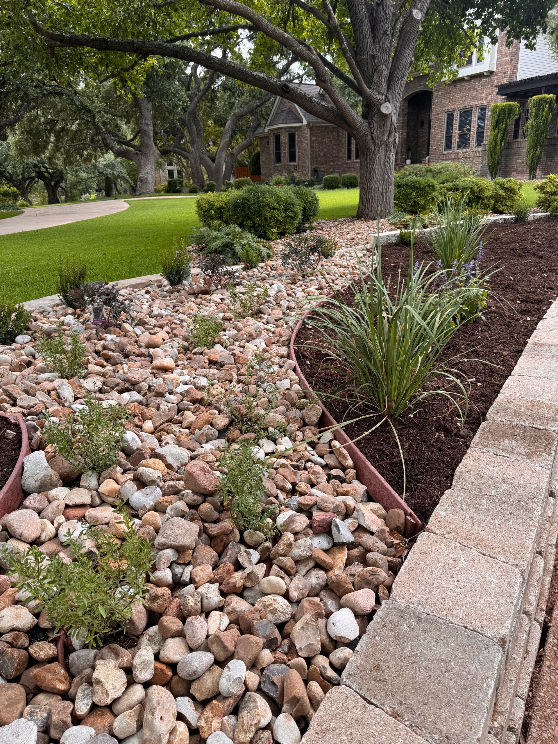 Landscaped front yard with rocks, mulch, plants, and a brick house.