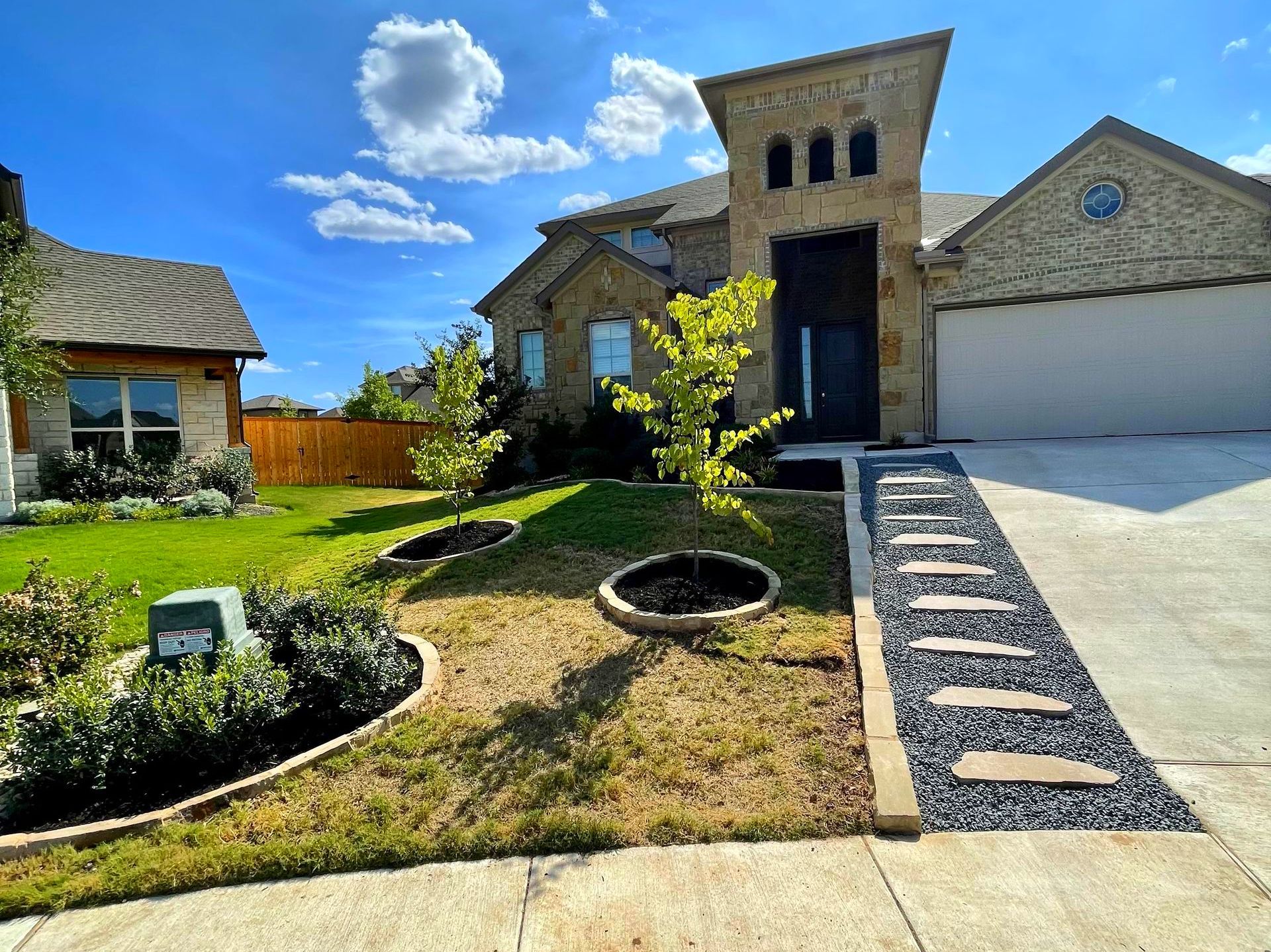 House exterior with stone facade, paved pathway, and landscaped lawn under blue sky.