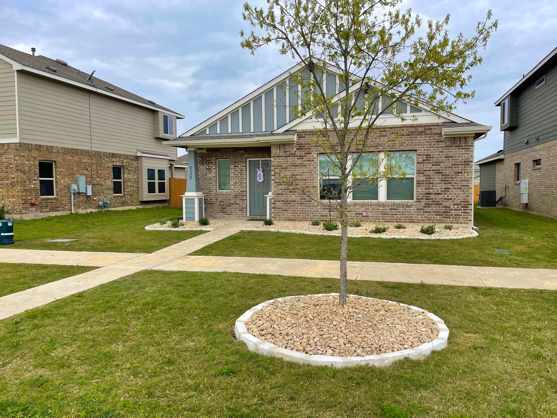 Brick home with green lawn, small tree in front yard, and neighboring houses.