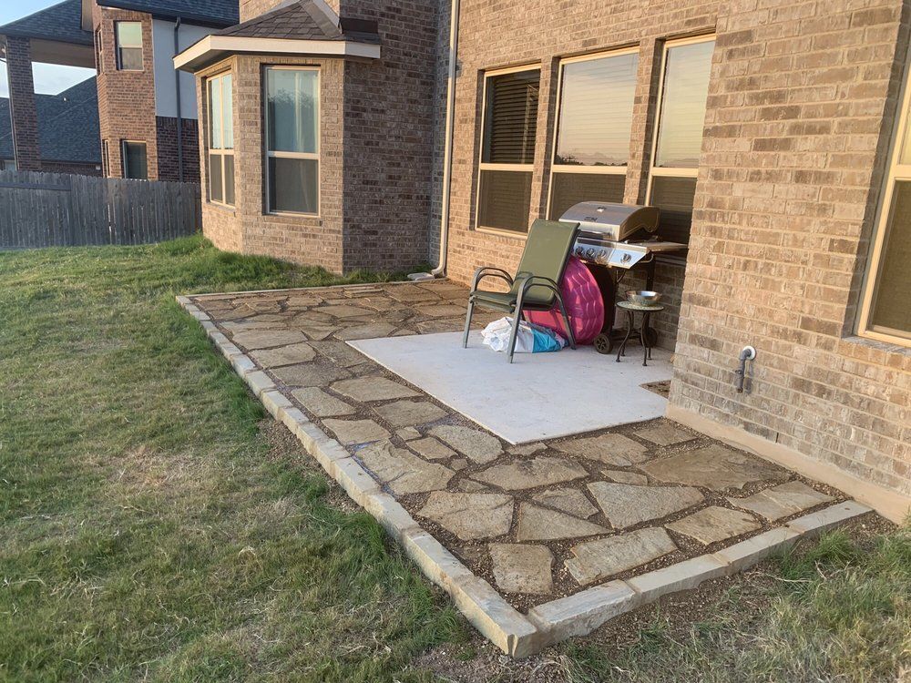 A flagstone patio next to a brick house with a grill and a chair.