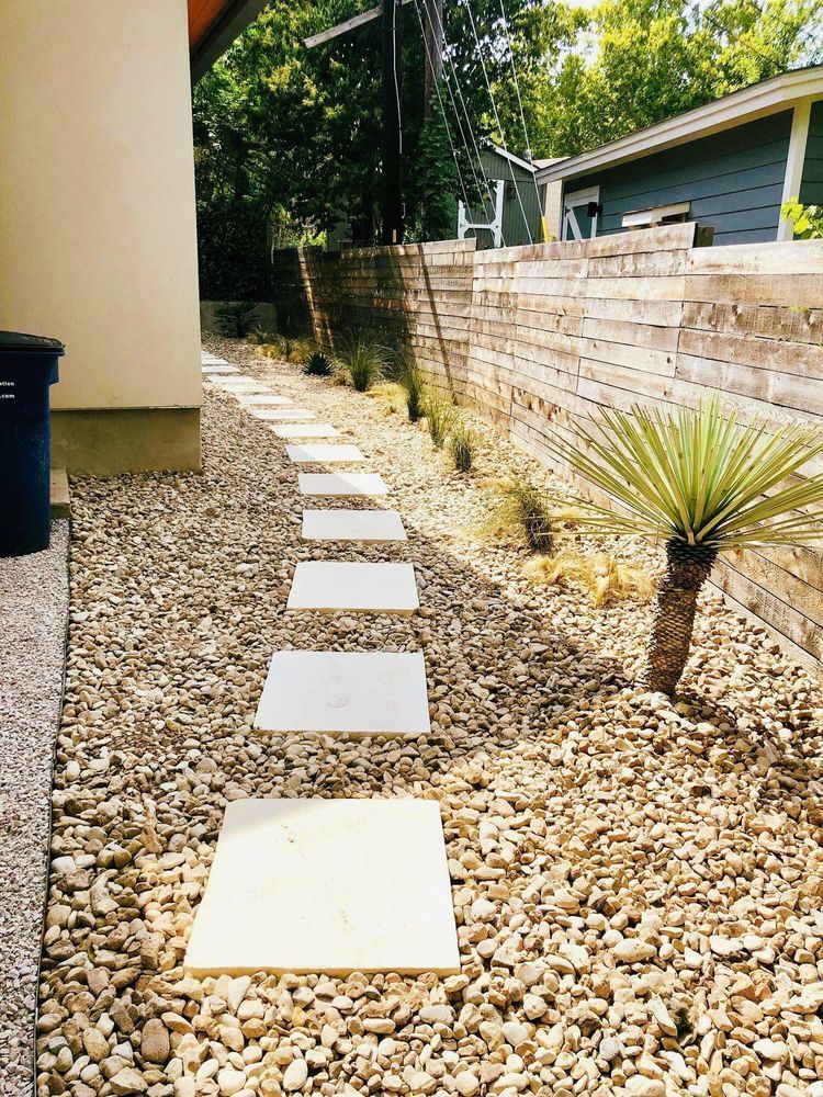 Stone path through gravel garden with small palm tree and wooden retaining wall.