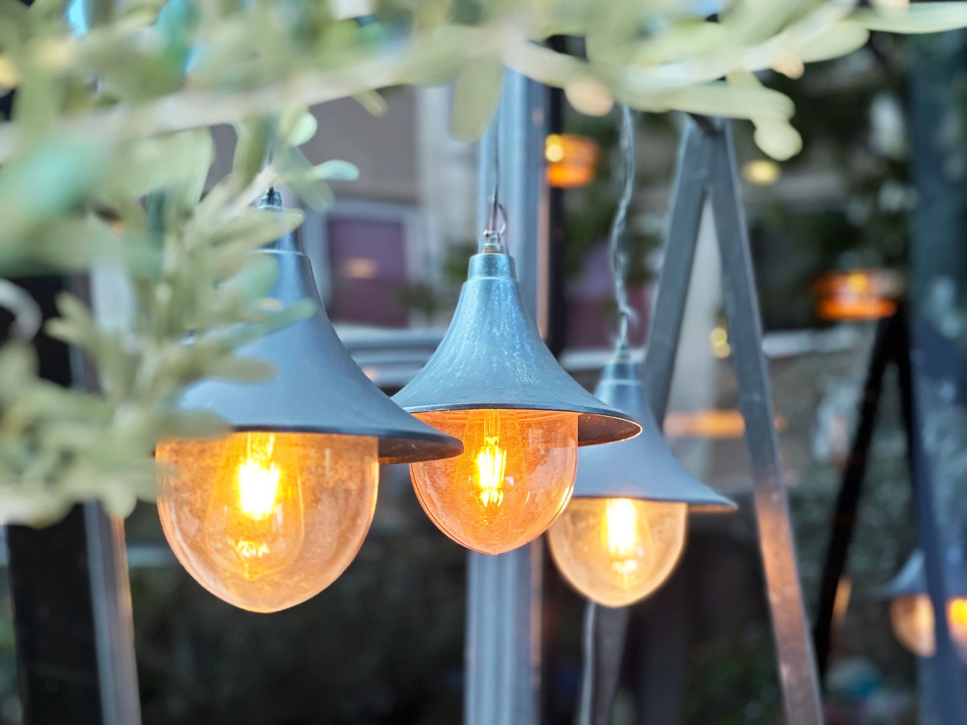 Three glowing outdoor pendant lights with a warm amber glow, blurred by foliage.