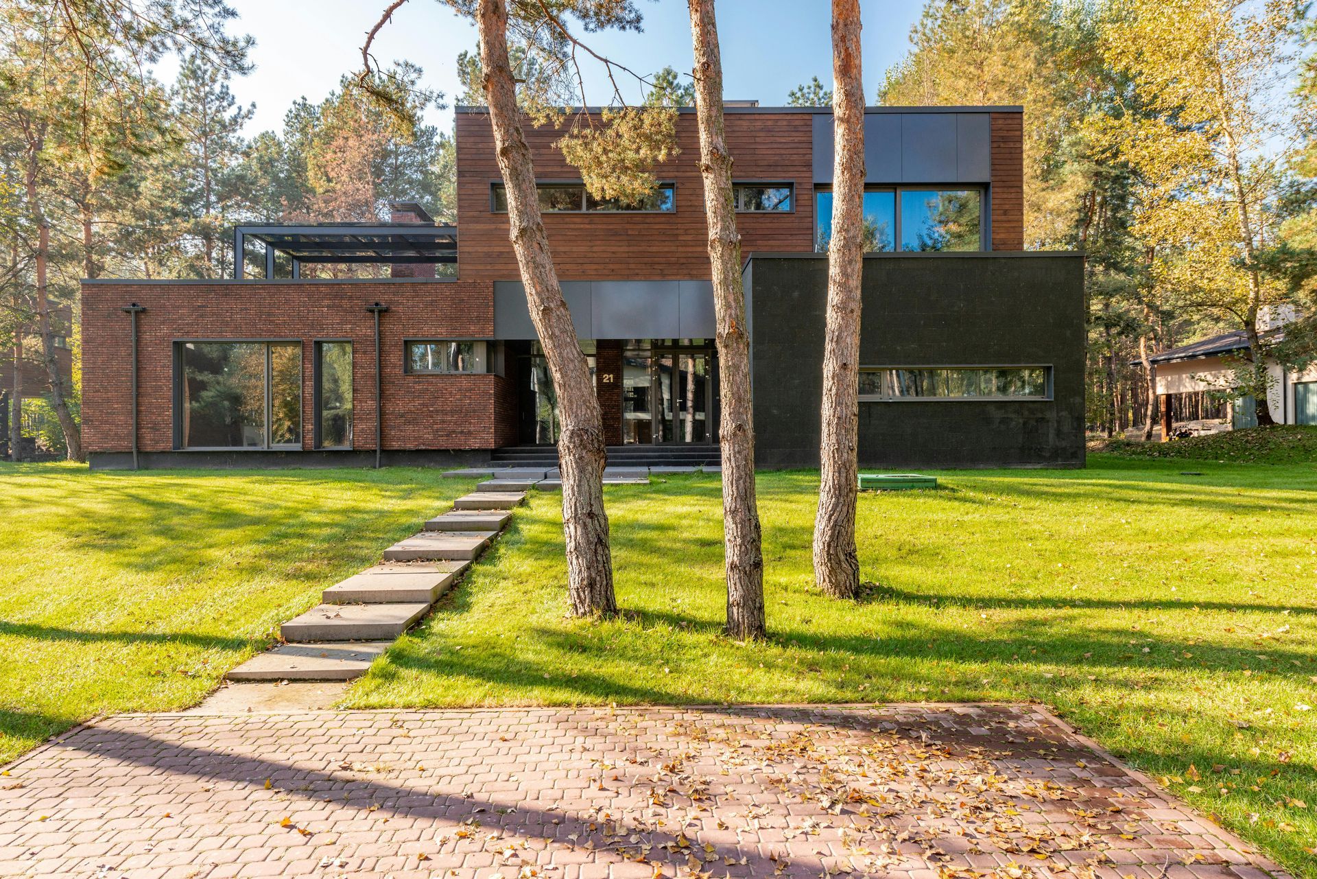 Modern home with brick and dark accents, trees in front, sunny yard.