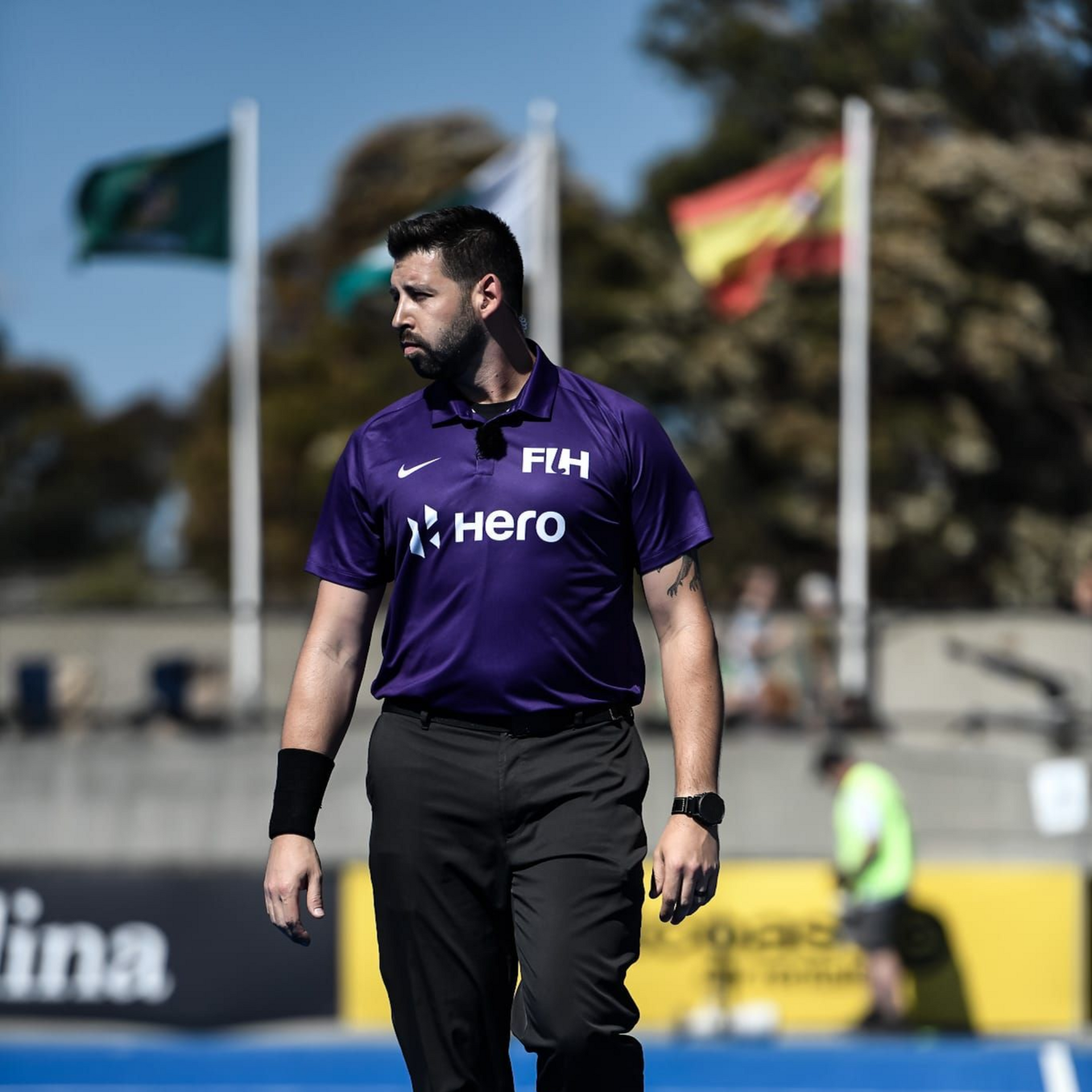 Field hockey umpire in purple shirt, watching the game on the blue field.