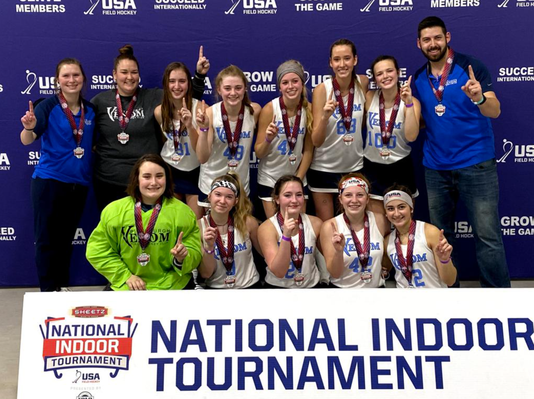 A group of people are posing for a picture in front of a national indoor tournament sign.