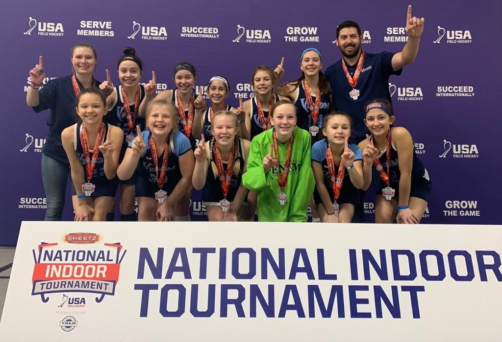 A group of people are posing for a picture in front of a sign that says national indoor tournament.