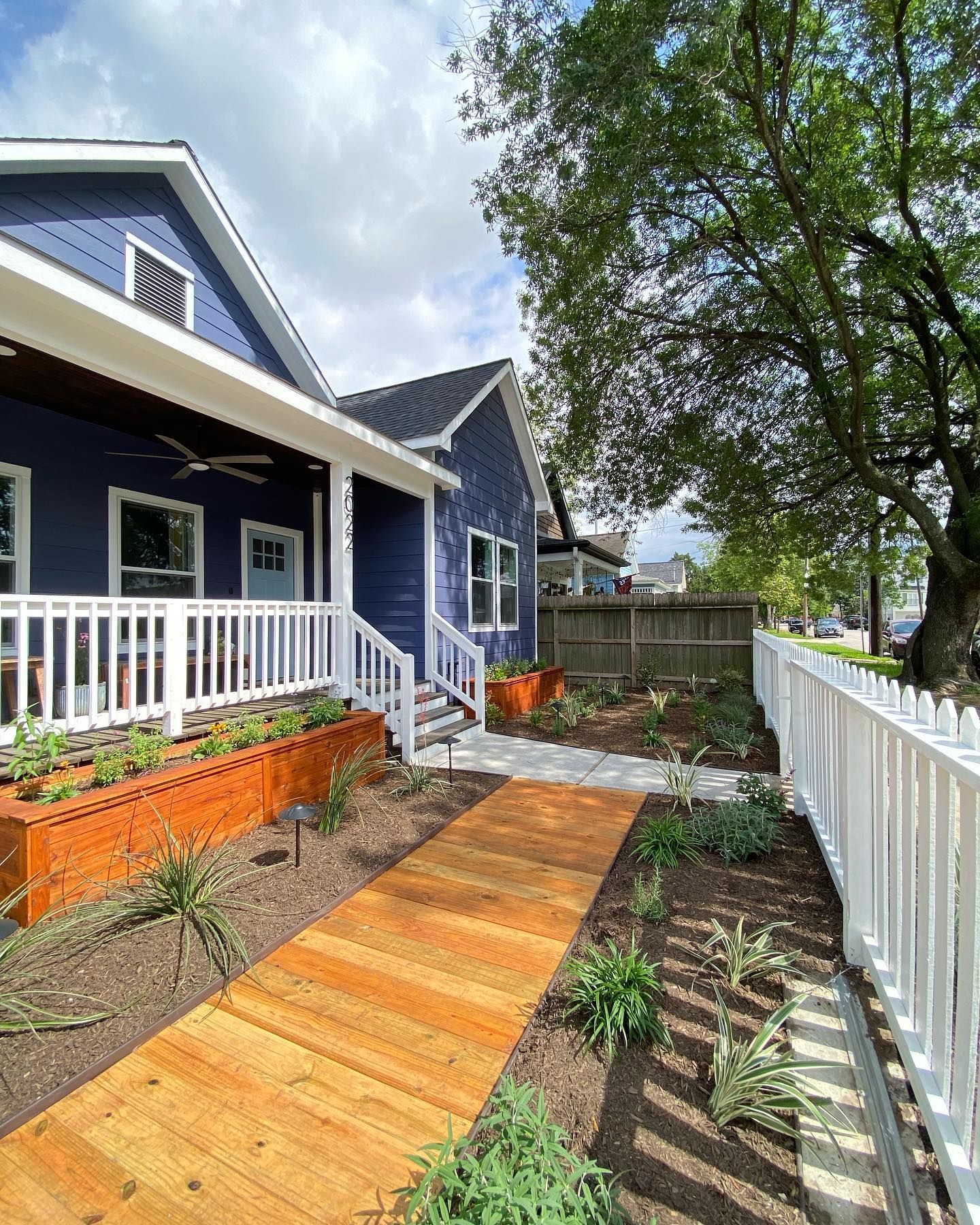 Blue house with a wooden walkway, a white picket fence, and a small garden.