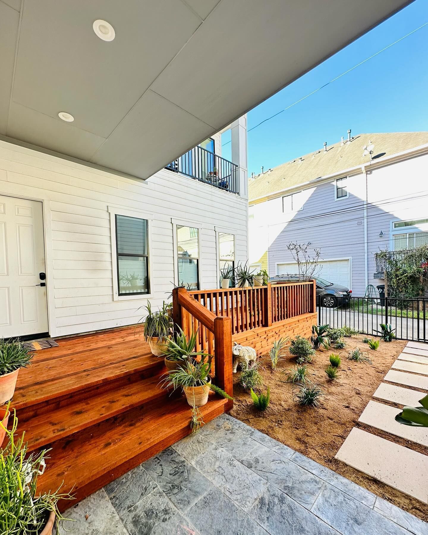 Wooden porch with steps leading to a white house with a gray roof overhang. Pathway of stone squares on the right.