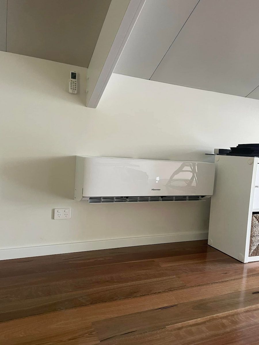 White Wall-mounted Air Conditioner in a Room With Slanted Ceiling and Hardwood Floor — Deltech HVACR in Port Stephens, NSW