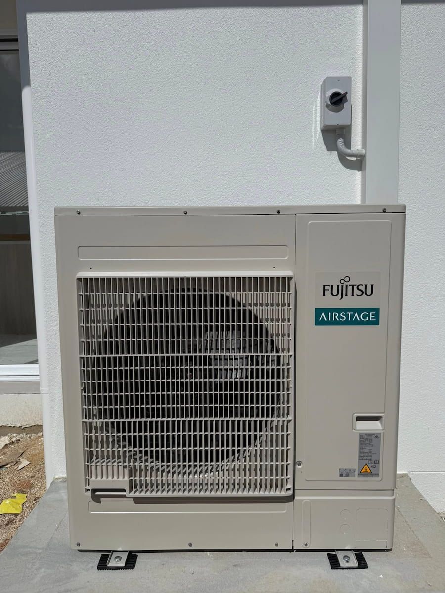 Outdoor Air Conditioner Unit Against a White Wall, With a Front Grille — Deltech HVACR in Lake Macquarie, NSW
