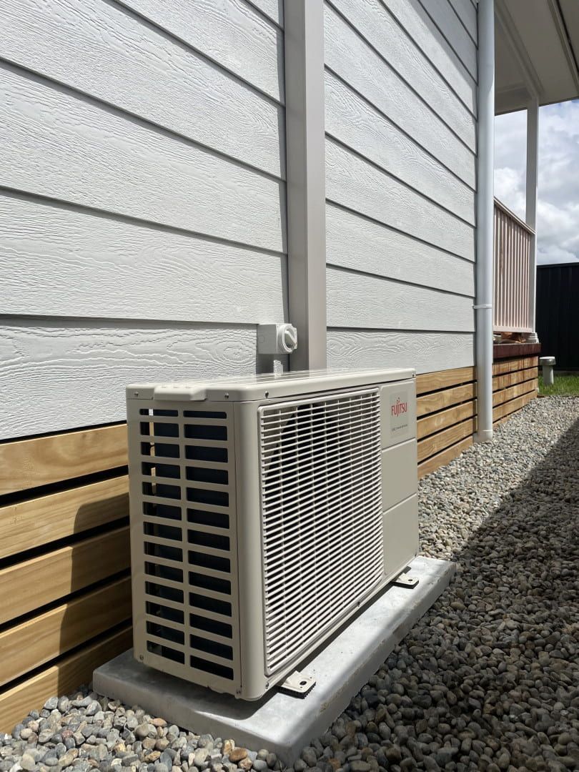 Outdoor Air Conditioner Unit Beside a White House Wall on Gravel Ground — Deltech HVACR in Cessnock, NSW