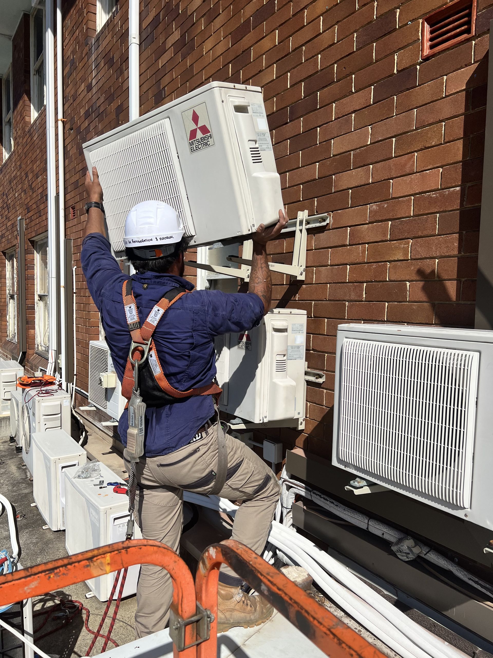 Worker installing an outdoor air conditioning unit on a brick building facade — Deltech HVACR in Georgetown, NSW