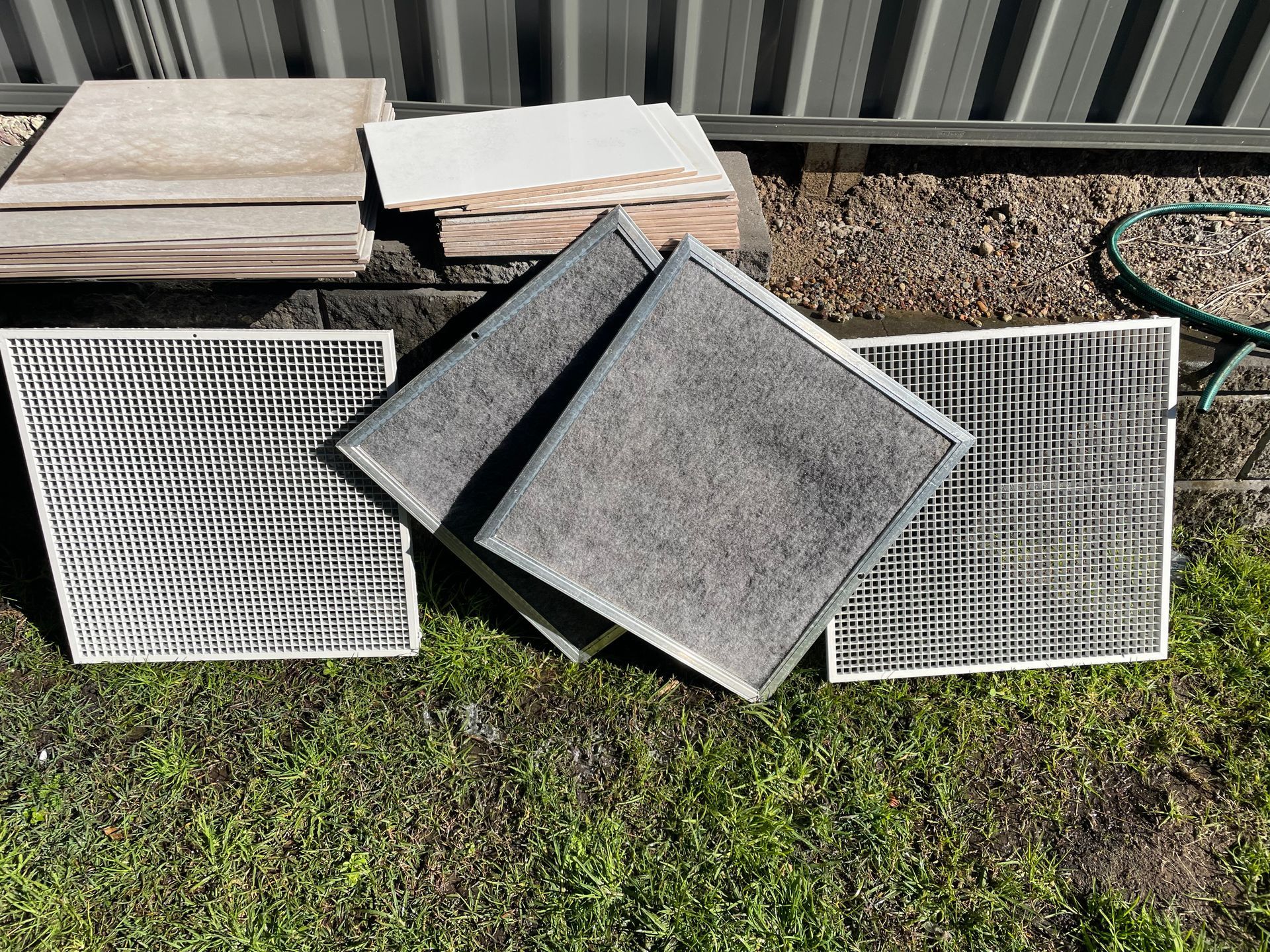 Several metal air filters and grates stacked outdoors on grass and gravel near a corrugated wall — Deltech HVACR in Georgetown, NSW
