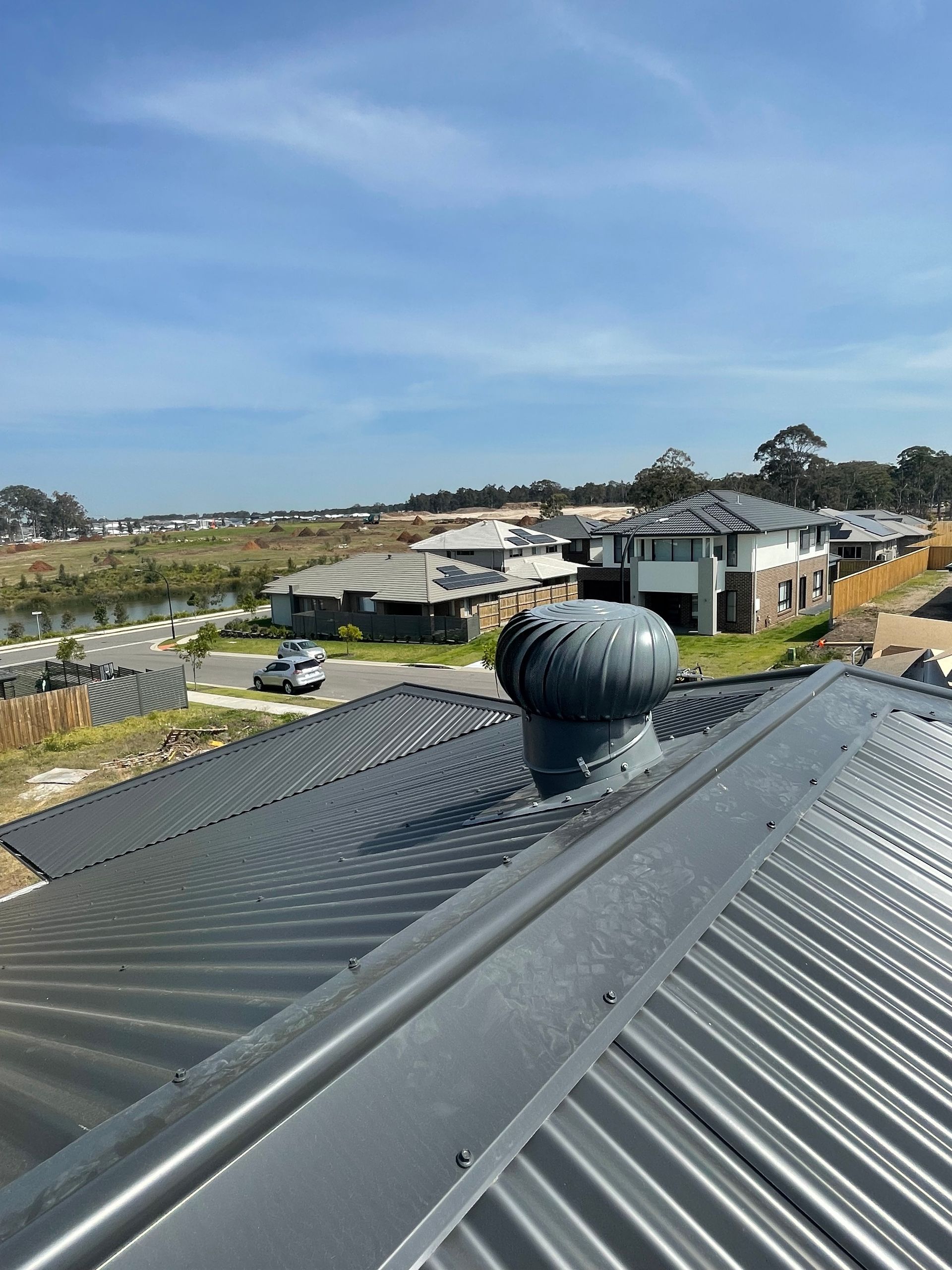 Rooftop With Dark Metal Vents Overlooking Houses and Trees Under a Blue Sky — Deltech HVACR in Georgetown, NSW