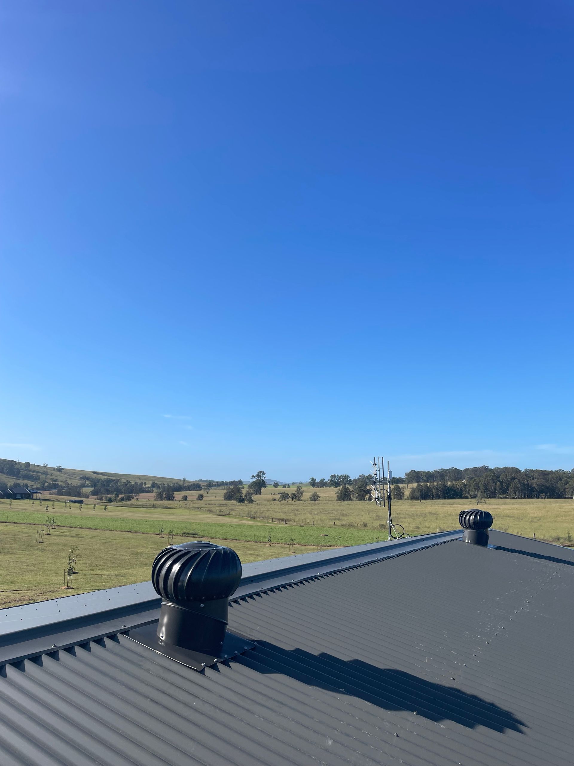 Rooftop With Black Vents Overlooking a Grassy Field Under a Clear Blue Sky — Deltech HVACR in Georgetown, NSW