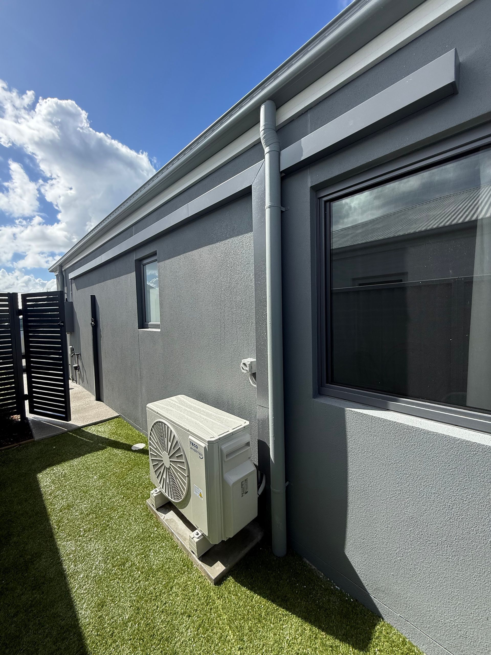 Gray house exterior with large windows, air conditioner unit, and grass along a side yard under a blue sky — Deltech HVACR in Georgetown, NSW