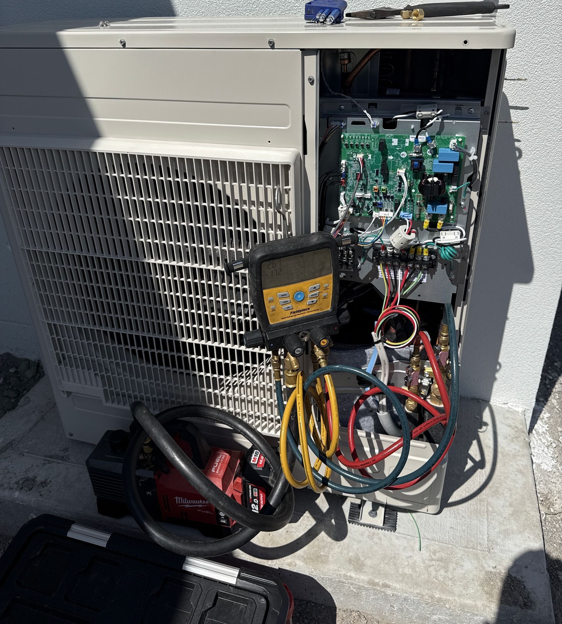 Open HVAC unit with exposed circuit board, multimeter, and tangled wires on a concrete surface — Deltech HVACR in Georgetown, NSW