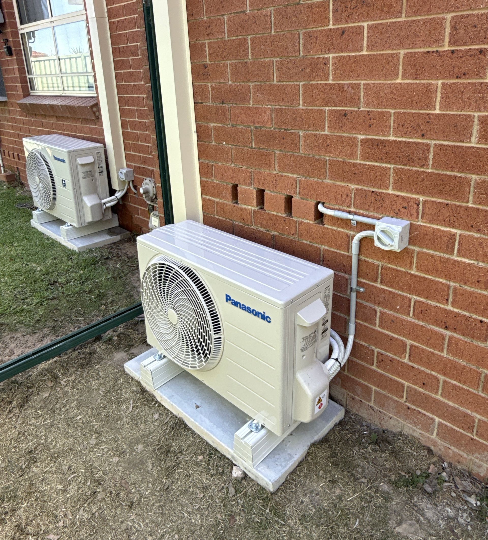 Two White Outdoor HVAC Units Beside a Brick Building Wall on Gravel Ground — Deltech HVACR in Central Coast, NSW