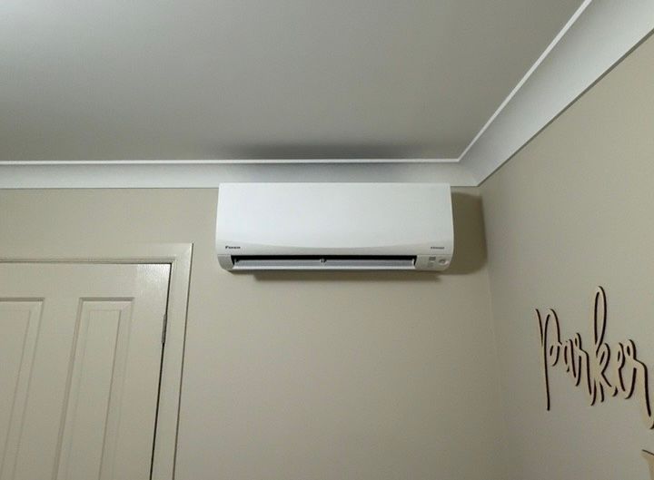 Wall-mounted white air conditioner on a beige room wall near the ceiling, beside a door — Deltech HVACR in Georgetown, NSW