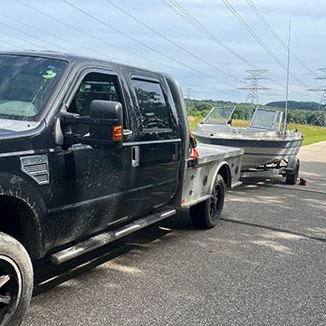 Black pickup truck towing a boat on a trailer; parked on pavement.