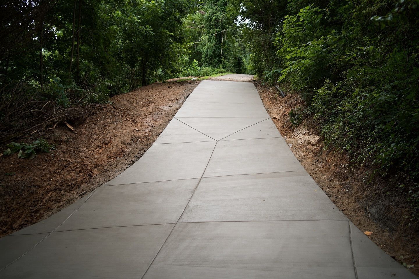 Concrete path through a wooded area. The path is grey and slopes upward.