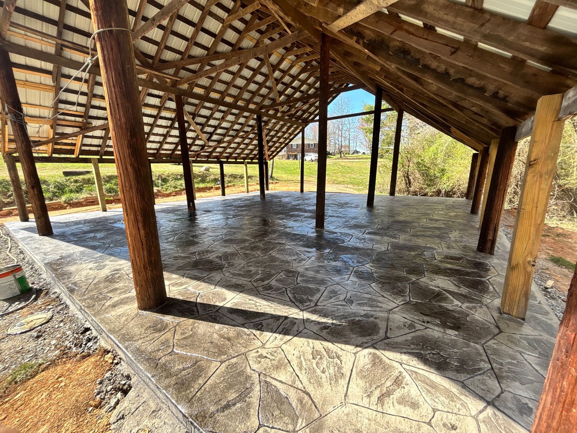 Wooden shelter with patterned concrete floor, brown support beams, and a grassy outdoor setting.