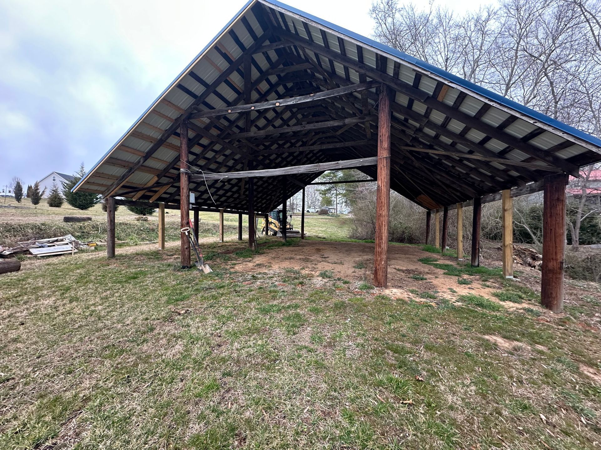 A long open-sided wooden shelter with a blue metal roof stands on a grassy area.