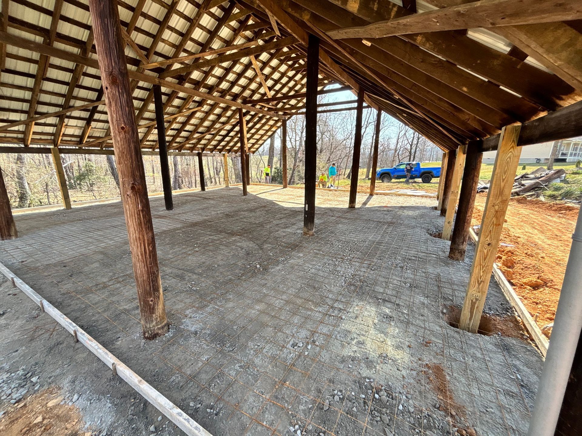 Open-air structure with gravel floor and wooden support beams, blue truck in the background.