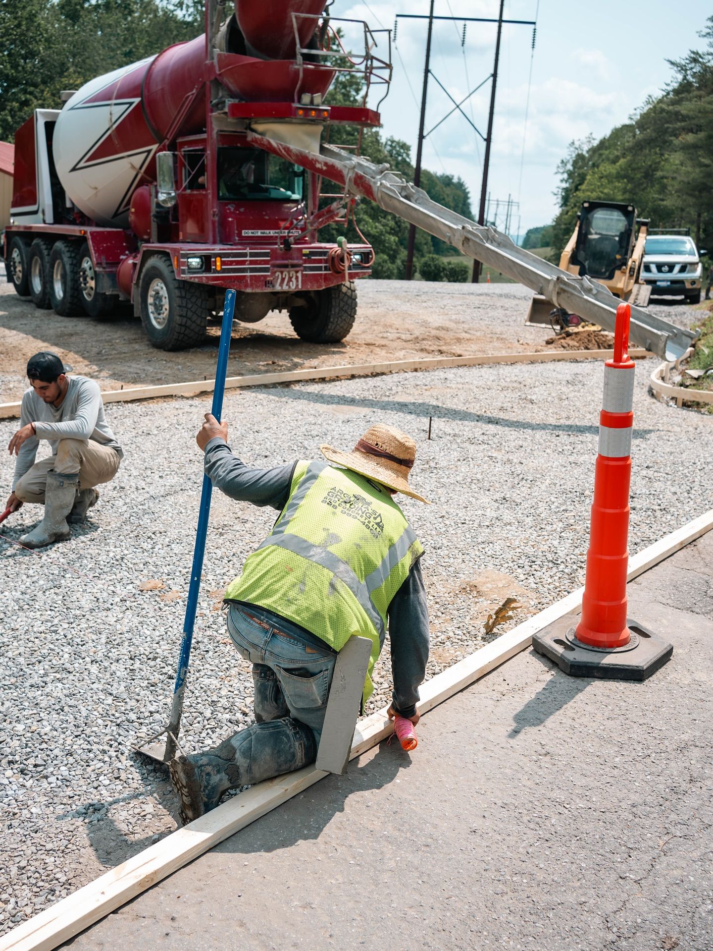 Construction workers pouring concrete from a truck. One levels the wet concrete with a tool.