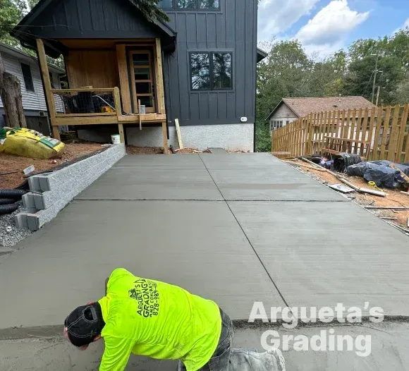 Person in neon green shirt finishing a freshly poured concrete driveway. Building and retaining wall in the background.