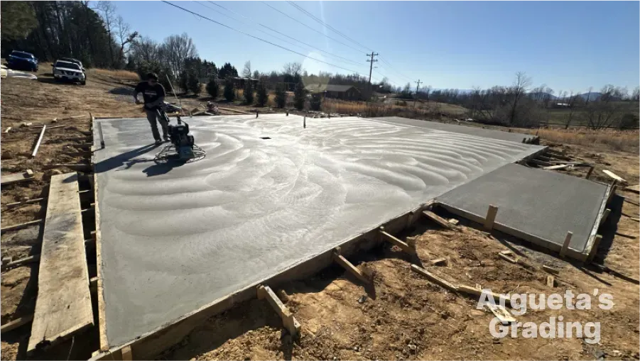 Man using a concrete grinder on a freshly poured concrete slab outdoors on a sunny day.