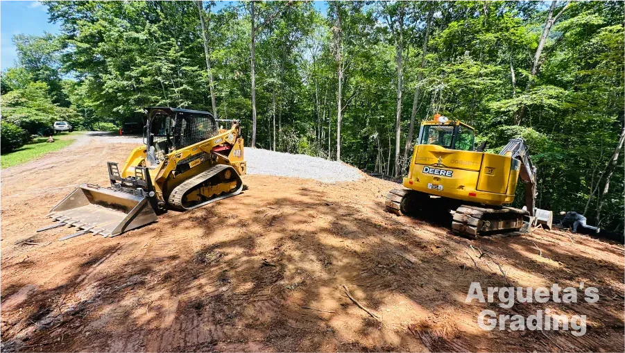 Two yellow construction vehicles on a dirt mound. Trees in the background. Arguta's Grading watermark.
